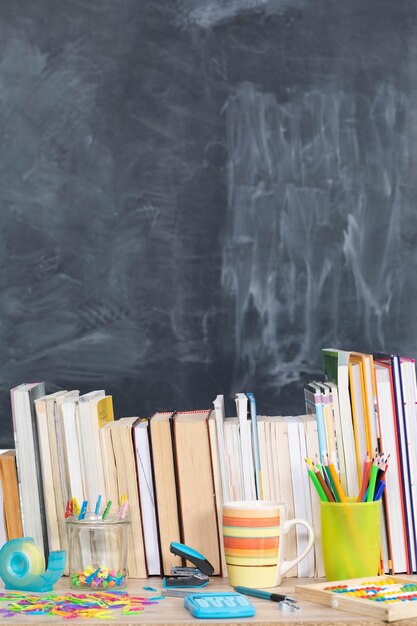 Derrière les livres, vous pouvez voir un tableau d'école. Beaucoup d'outils scolaires sont disposés sur le bureau.