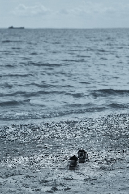Désespoir impuissance tristesse solitude concept Hot day hot concept Chaussures noires laissées sur la plage L'homme ou la femme a enlevé ses chaussures et est allé dans la mer Grain de film