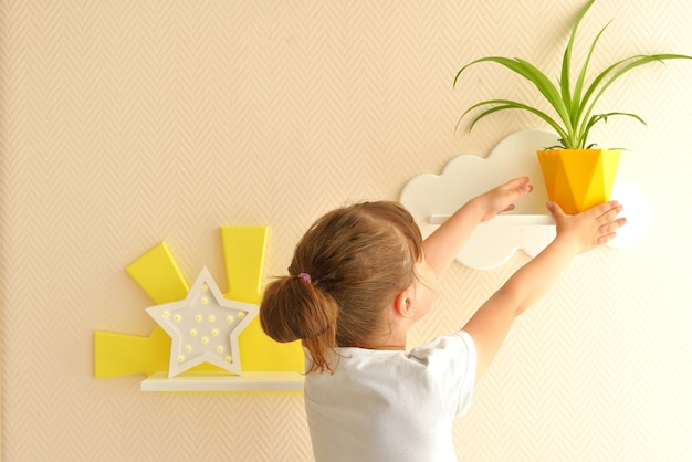 Design d'intérieur élégant et moderne. Accueil pour la chambre d'enfant. fille met un pot jaune sur l'étagère. Étagères pour enfants en forme de nuages blancs sur un mur beige uni.