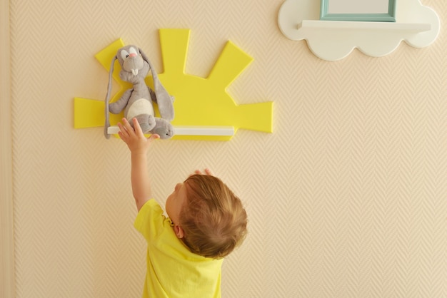 Design d'intérieur élégant et moderne. Accueil pour la chambre d'enfant. un petit garçon prend une peluche de lièvre gris sur l'étagère.