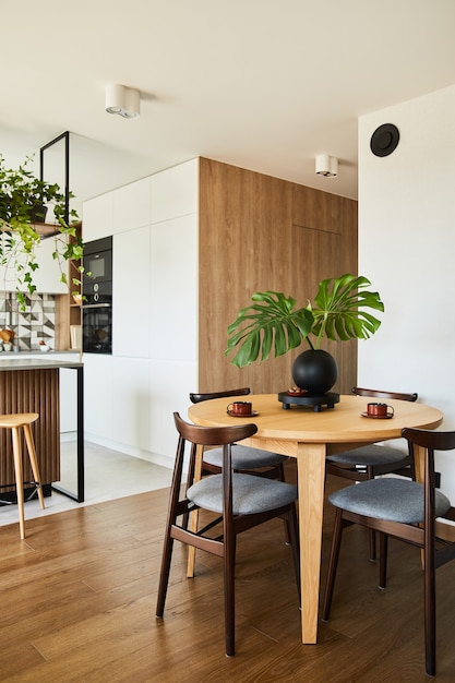 Design d'intérieur élégant de salle à manger avec table à manger. Espace de travail avec accessoires de cuisine en arrière-plan. Murs créatifs, panneaux blancs et bois. Style minimaliste un concept d'amour végétal.