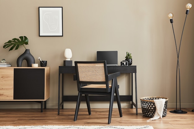 Design d'intérieur de fantaisie de l'espace de bureau à domicile avec une chaise élégante, un bureau, une commode, un cadre noir, un ordinateur portable, un livre, un organisateur de bureau et d'élégants accessoires de décoration dans la décoration intérieure.