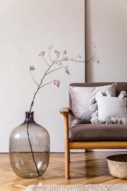 Design intérieur moderne du salon avec canapé en bois marron, oreillers, panier en rotin, vase en verre avec fleurs et accessoires élégants. Concept beige et japandi. Un home staging élégant.