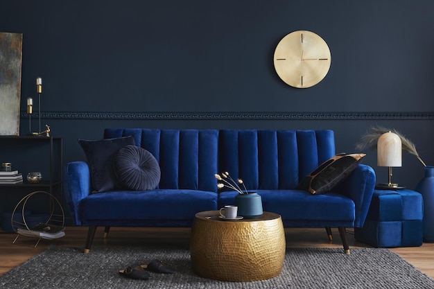 Design d'intérieur de salon moderne et élégant avec canapé en velours bleu glamour pouf étagère en métal noir affiche plantes et accessoires de maison modernes Modèle de mur bleu foncé Espace de copie