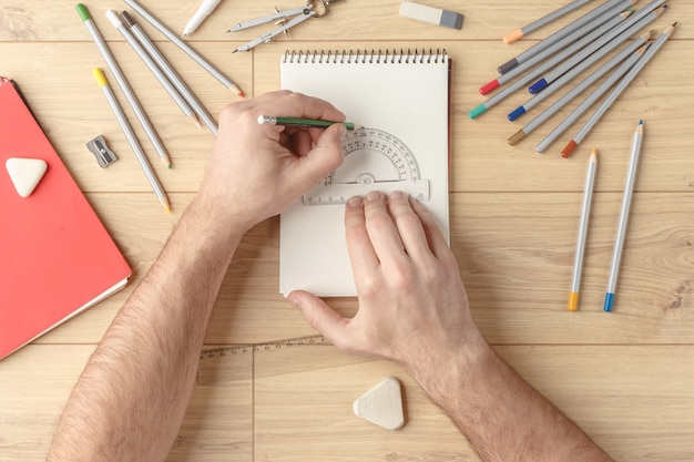 Le designer dessine un croquis dans un cahier sur une table en bois. Papeterie. Vue d&#39;en-haut.