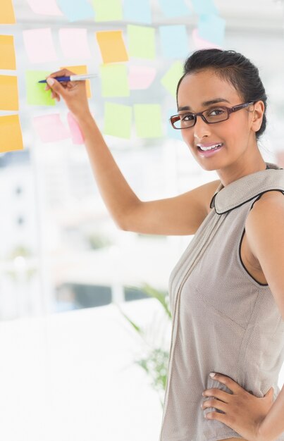 Designer d&#39;écriture sur des notes autocollantes sur la fenêtre, souriant à la caméra