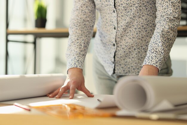 Une designer féminine se tient près de son bureau avec des rouleaux de papier architecte travaille en elle