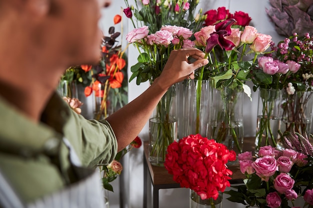 Designer floral debout à côté de la table avec des vases à fleurs et sortant une seule fleur de l'eau