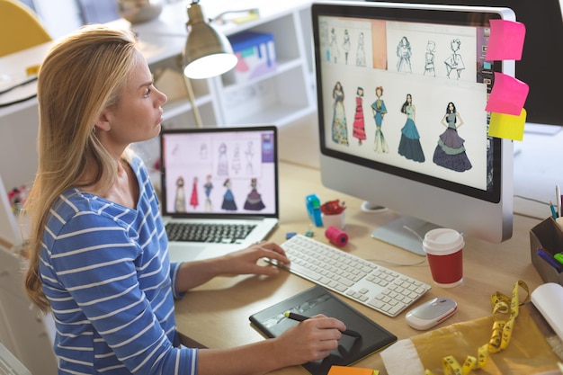 Designer de mode féminine utilisant une tablette graphique tout en travaillant à son bureau