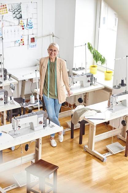 Designer avec ruban à mesurer se penche sur table avec machine à coudre dans un atelier bien éclairé