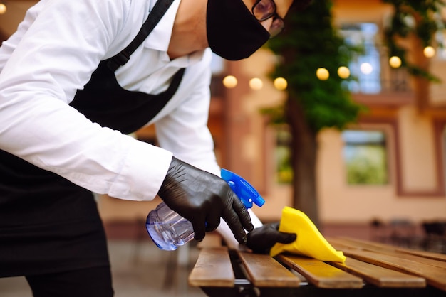 Désinfecter pour prévenir le COVID19 Serveur nettoyant la table avec un spray désinfectant