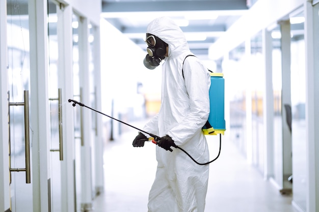 Désinfection du bureau pour prévenir le COVID-19, Homme en combinaison de protection contre les matières dangereuses avec des produits chimiques en aérosol.