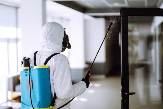 Désinfection du bureau pour prévenir COVID19 Homme en combinaison de protection contre les matières dangereuses avec des produits chimiques en aérosol