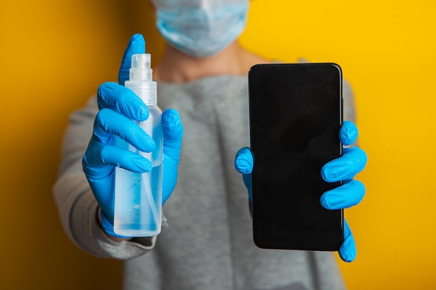 Désinfection du téléphone. Une femme dans un masque médical et des gants en caoutchouc tient un téléphone et un désinfectant en spray dans ses mains.