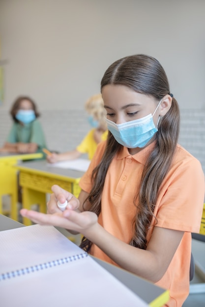 Désinfection. Fille dans un masque désinfectant ses mains avant la leçon