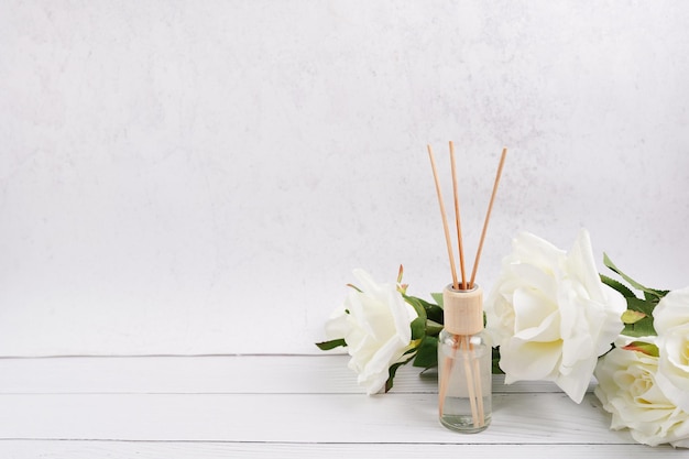 Photo désodorisant aromatique de roseau, bouteille de diffuseur de parfum avec des bâtons d'arome avec la fleur rose sur le fond blanc de mur