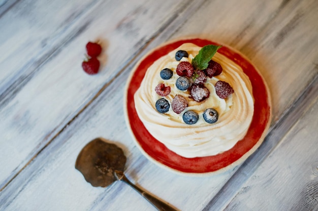 Dessert Anna Pavlova aux framboises et bleuets sur une surface en bois blanche