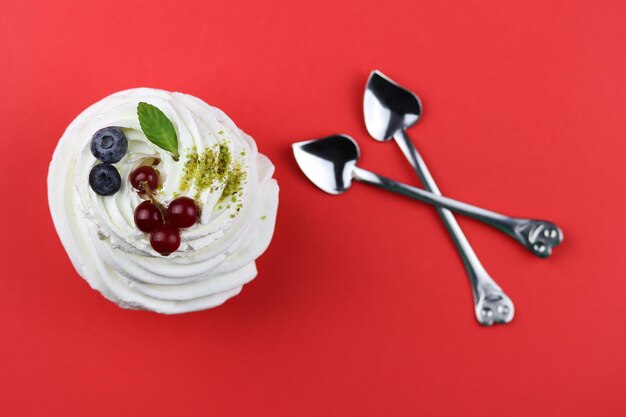 Dessert d'Anna Pavlova avec des baies et des feuilles de menthe sur fond rouge avec des cuillères en forme de coeur à proximité