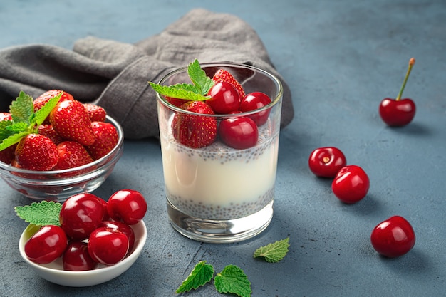 Dessert au lait avec graines de chia et cerises et fraises fraîches sur fond bleu foncé. Vue latérale, gros plan.