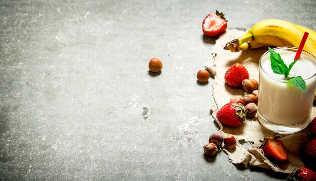 Dessert au lait avec des noix, des baies et des bananes. Sur la table en pierre.