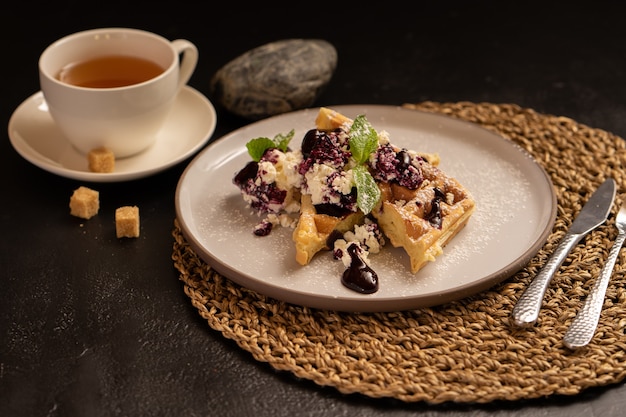 Dessert au thé. Les gaufres viennoises au fromage cottage, à la menthe et à la confiture de baies sont magnifiquement conservées avec une tasse de thé et de la cassonade.