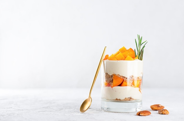 Dessert au verre avec du persimmon, du romarin, de la crème aux noix de pécan et une cuillère de sucre végétalien sans gluten et lactose