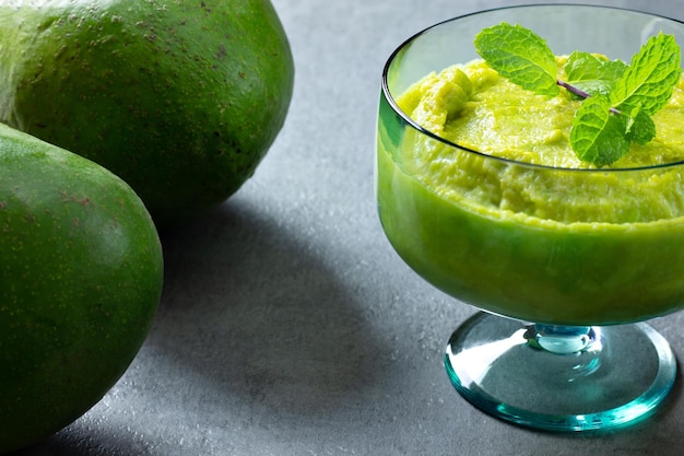 Dessert à l'avocat dans un bocal en verre vert avec de la menthe sur le dessus à côté d'avocats entiers sur fond gris