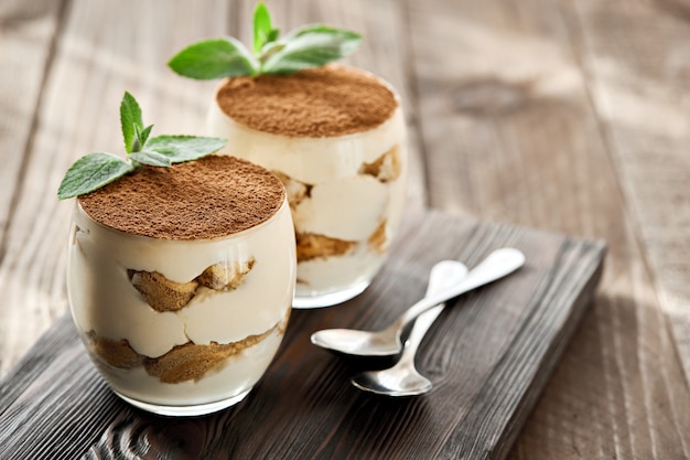 Photo dessert classique tiramisu dans un verre sur une planche de bois par une journée ensoleillée