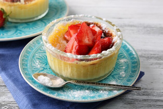 Dessert crème brûlée avec des baies de fraises fraîches sur une serviette sur fond de bois de couleur