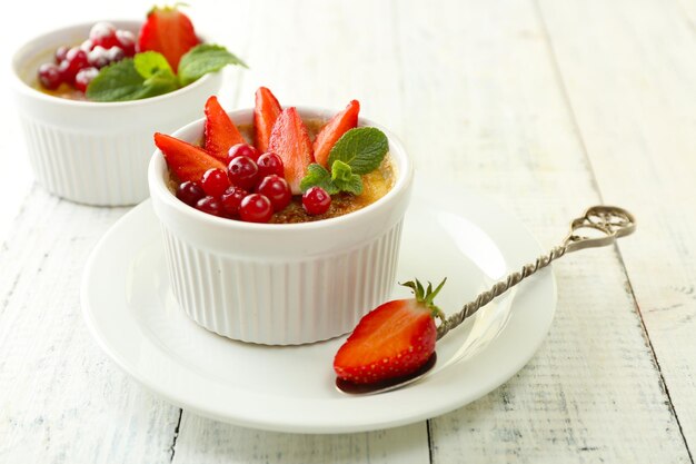 Dessert crème brûlée avec des fraises fraîches et des feuilles de menthe sur fond de bois de couleur