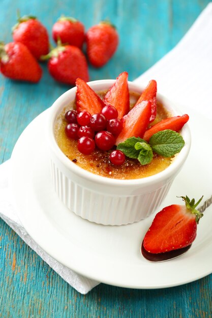 Dessert crème brûlée avec des fraises fraîches et des feuilles de menthe sur fond de bois de couleur