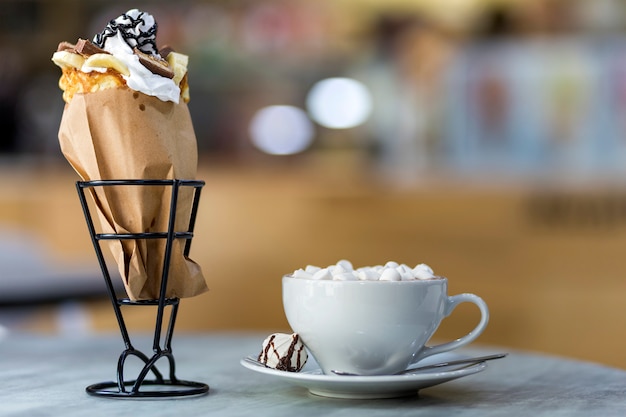 Photo dessert de crème glacée dans une tasse de gaufrette avec des biscuits au chocolat et une tasse de café avec des guimauves sur une assiette en porcelaine sur fond d'espace copie colorée floue.