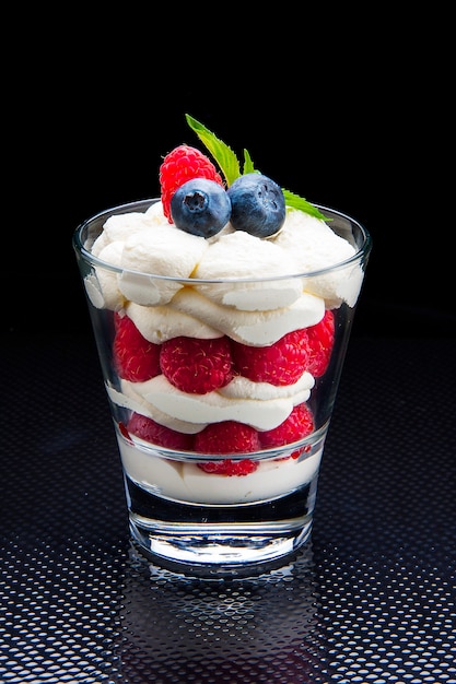 Dessert dans un verre avec des framboises fraîches et des morceaux de biscuit