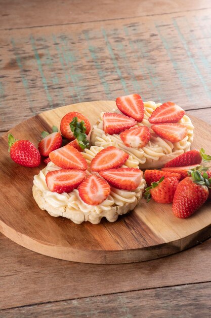 Dessert de deux gaufres avec de la crème au chocolat blanc et des morceaux de fraises sur une planche de bois ronde et des fraises coupées sur une vue d'angle de table en bois