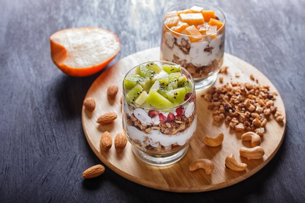 Dessert avec du yaourt grec, granola, amande, noix de cajou, kiwi et kaki sur fond en bois.