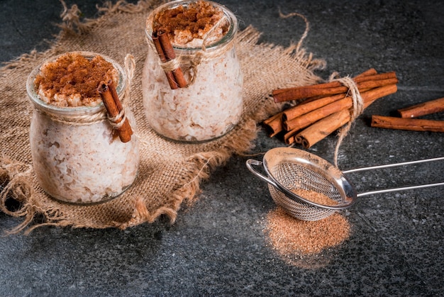 Dessert espagnol, sud-américain et mexicain. Bouillie sucrée, riz au lait. Riz au lait. En pots portionnés, décorés de cannelle et de sucre. Sur une table en pierre sombre. Espace copie