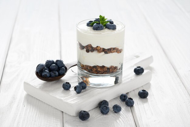 Dessert avec fromage cottage bleuets frais et granola dans un verre sur un fond en bois blanc