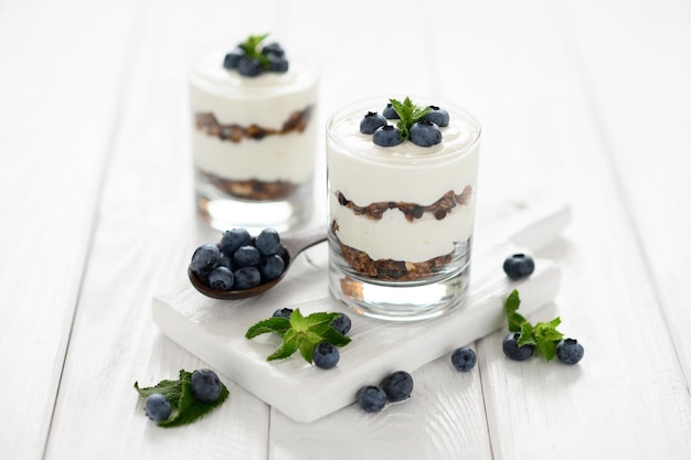 Dessert avec fromage cottage bleuets frais et granola dans un verre sur un fond en bois blanc