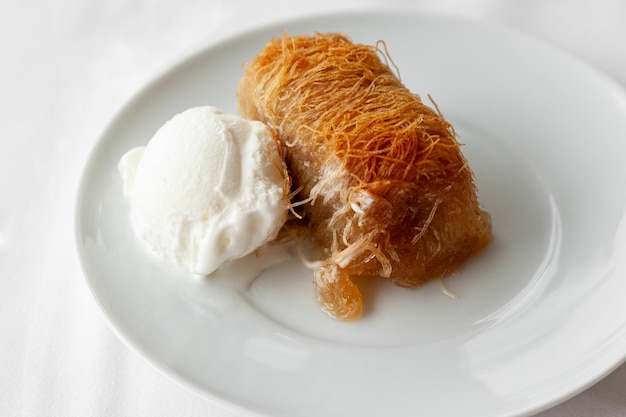 Photo un dessert grec traditionnel, le kataifi, servi avec de la crème glacée sur une assiette blanche.