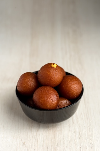 Dessert indien ou plat sucré: Gulab Jamun dans un bol sur fond de bois.