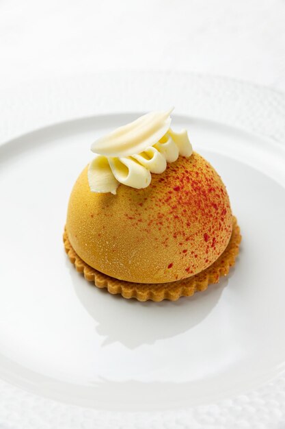 Un dessert jaune avec un glaçage blanc et des vermicelles rouges sur le dessus.