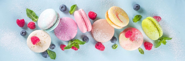 Dessert macaron français coloré. Ensemble de différents goûts et biscuits macaron de couleur avec des baies, du sucre en poudre et de la menthe sur fond bleu