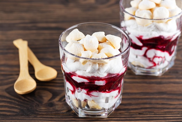 Dessert maison avec crème de noix de coco meringuée aquafaba et cerises dans des verres sur une table en bois