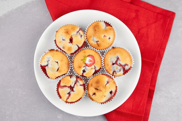 Dessert muffin aux fraises sur plaque blanche sur serviette en lin rouge sur fond de table gris, vue du dessus