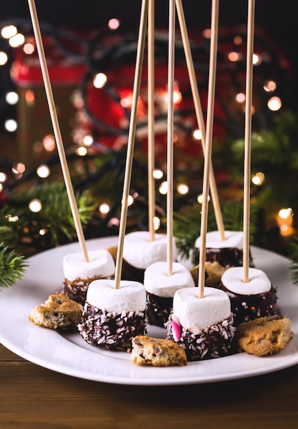 Photo dessert de noël ou une collation de guimauve au chocolat sur une assiette blanche des lumières de noël des aliments de vacances