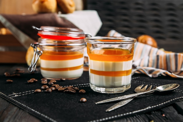 Dessert panacotta aux pêches dans un pot sur un fond sombre avec des éléments décoratifs, vue latérale, horizontal