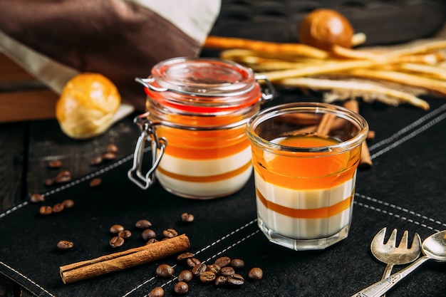 Dessert panacotta aux pêches dans un pot sur un fond sombre avec des éléments décoratifs, vue latérale, horizontal