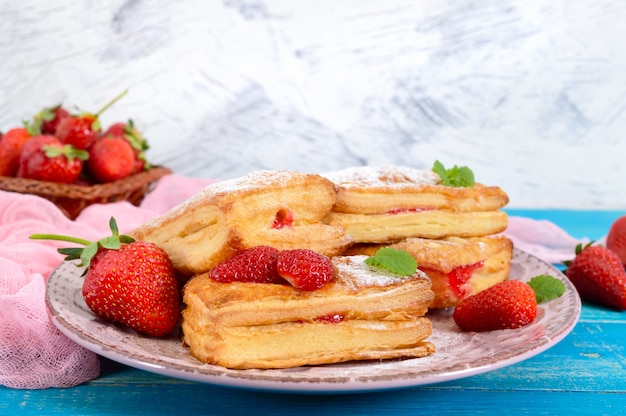 Dessert de pâte feuilletée savoureuse sucrée sur une plaque sur un fond en bois. Délicieux biscuits maison avec confiture de fraises, baies et sucre en poudre