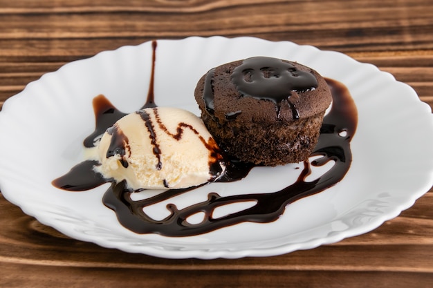 Dessert de petit gâteau avec la crème glacée et le sirop de chocolat sur le fond en bois