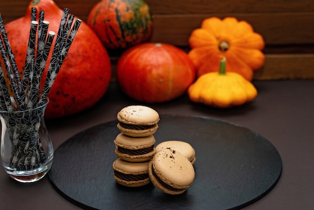 Dessert pour Halloween. Menu de l'Action de grâce. macarons français. Macarons au chocolat sur fond noir avec des citrouilles et des pailles à cocktails écologiques. Mise au point sélective douce.